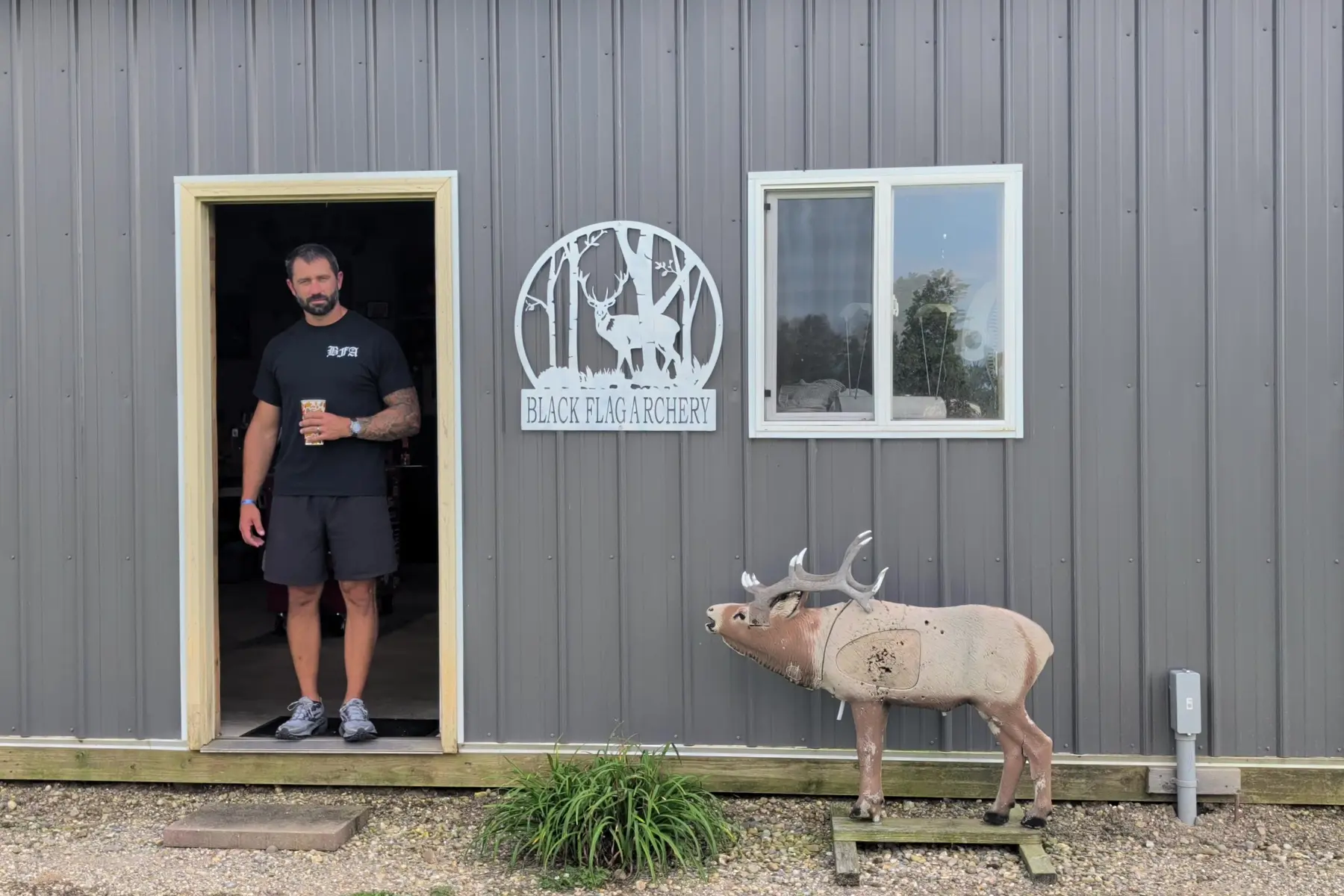Willy T. wearing Black Flag Archery merch in the shop entrance beside the Black Flag sign
